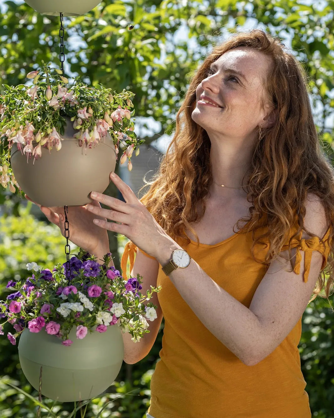 Vrouw in een geel shirt lacht naar een hangende Globee met bloemen in haar tuin